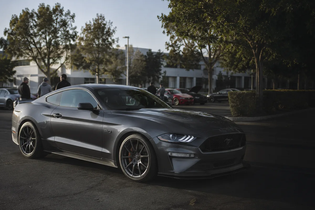 A crowd of enthusiasts around a modified Mustang GT at a meet